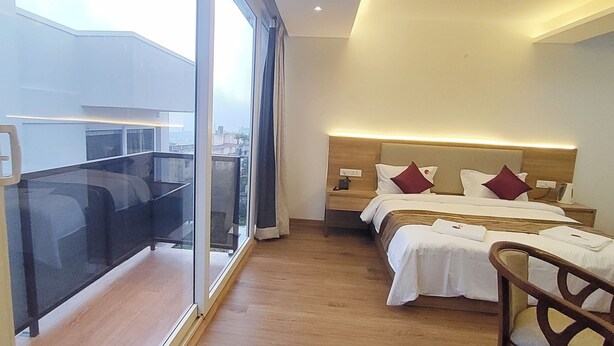 A hotel room with a balcony, a bed with two pillows, a bedside table, and a chair. - Spring Valley Enclave (Kodaikanal)