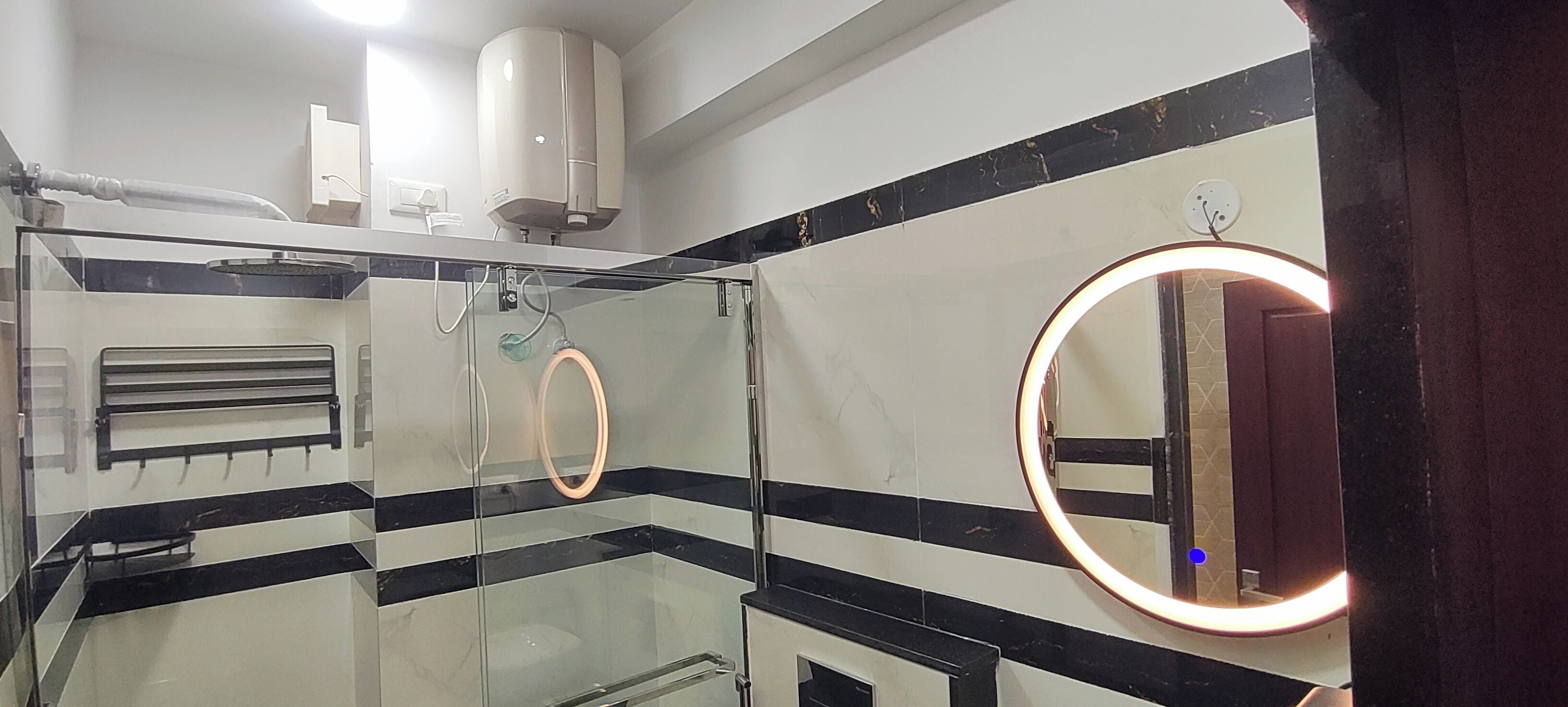 Une salle de bain moderne dotée d’une paroi en verre, d’un porte-serviettes, d’un miroir avec éclairage intégré et d’un purificateur d’air fixé au plafond.