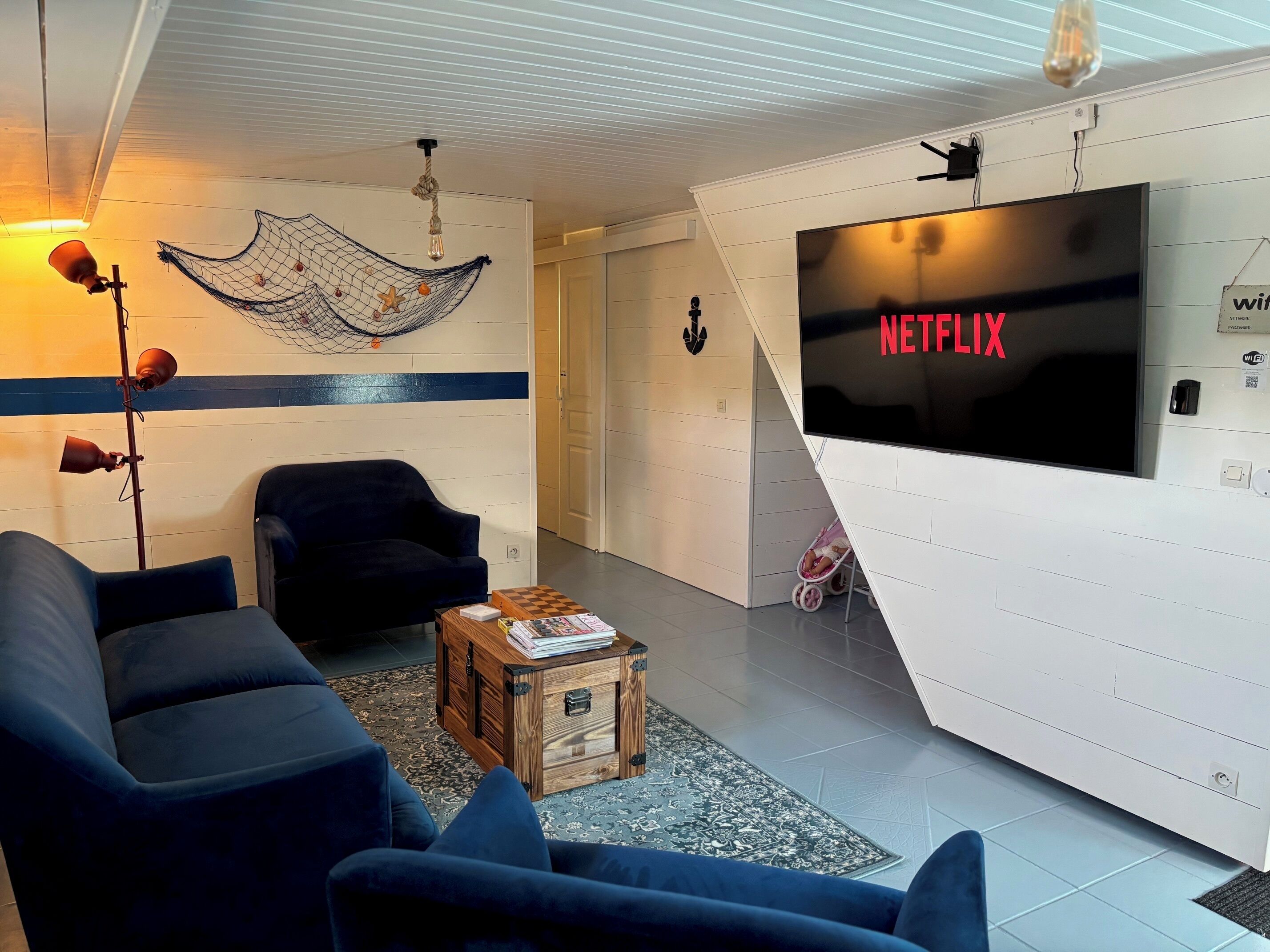 A modern living room with a large flat-screen TV displaying "NETFLIX," a cozy sofa, a small wooden coffee table, and a hammock with decorative items.