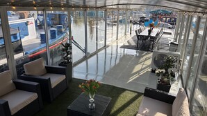 A covered outdoor seating area with wicker furniture, a small table with a vase of flowers, and a view of boats and docks through large glass windows. - Entire bungalow for family or friends up to 15 people, terrace, unique! (Hlavní město Praha)