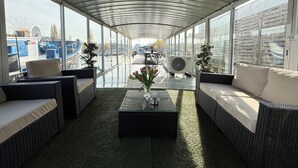 A covered outdoor seating area with wicker furniture, a central table with a vase of flowers, and large windows offering views of the surrounding area. - Entire bungalow for family or friends up to 15 people, terrace, unique! (Hlavní město Praha)