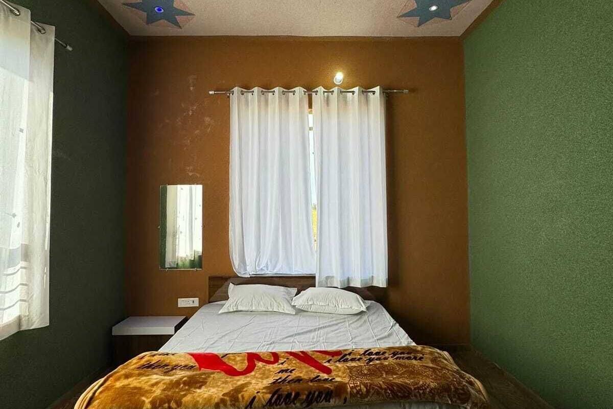 A bedroom with a bed, a nightstand, a mirror, and a window with curtains.