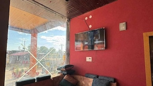 A corner sofa with a wooden floor, a red wall, and a TV mounted above it. - Hotel Raghukul (Shri Madhopur)