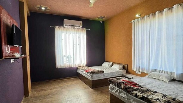 A bedroom with two beds, a ceiling fan, an air conditioner, and a window with curtains. - Hotel Raghukul (Shri Madhopur)