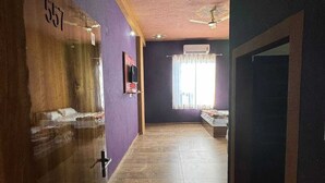A hallway with purple walls, a wooden door labeled '557', a ceiling fan, and a window with curtains. - Hotel Raghukul (Shri Madhopur)
