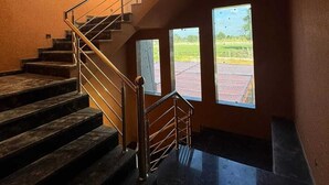 A staircase with metal railings and wooden steps leading to a landing with large windows. - Hotel Raghukul (Shri Madhopur)