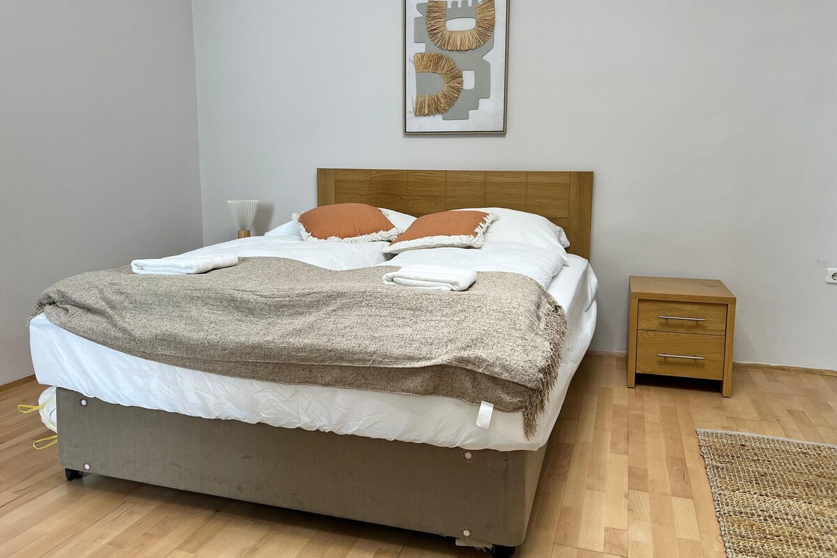 A neatly made bed with a wooden headboard, a bedside table, and a wall-mounted artwork.
