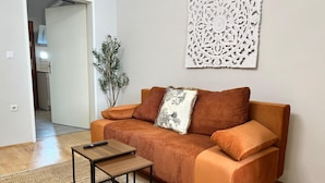 A living room with a sofa, a small table, a plant, and a decorative wall piece. - Lovely Studio for 4 with Garden (Vienna)