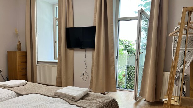 A bedroom with a bed, a TV mounted on the wall, a wooden dresser, and a window with curtains. - Lovely Studio for 4 with Garden (Vienna)