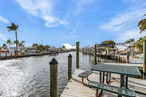 A waterfront dock with wooden posts, a green picnic table, and a row of palm trees. - Waterfront Cottage Retreat in St. James City — Brand New 1BR/1BA with Private Dock & Boat Lift (Saint James City)