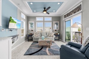 A spacious living room with a ceiling fan, a grey sofa, a coffee table, and a TV mounted on the wall. - Waterfront Cottage Retreat in St. James City — Brand New 1BR/1BA with Private Dock & Boat Lift (Saint James City)