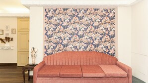 A room with a floral wallpaper, a pink sofa, and a small table with decorative items. - Enjoyable 2-bedroom apartment with AC in vibrant Kolkata (Kolkata)