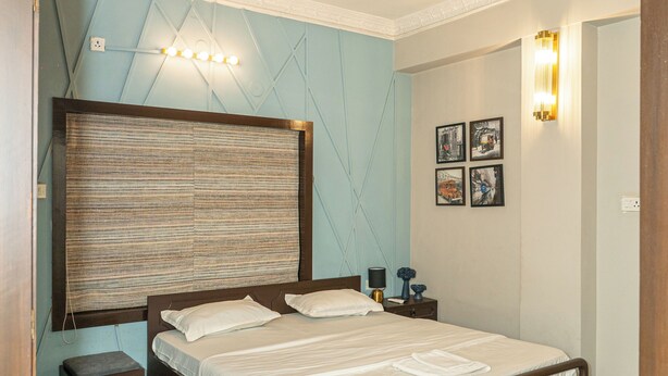 A bedroom with a wooden bed, a ceiling fan, a nightstand, a bedside table, and a wall-mounted light fixture. - Enjoyable 2-bedroom apartment with AC in vibrant Kolkata (Kolkata)