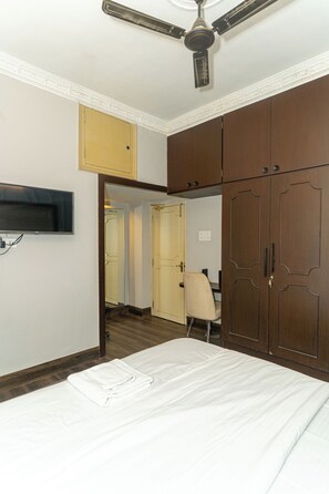 Een slaapkamer met een bed, een plafondventilator, een kledingkast en een aan de muur bevestigde televisie.