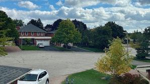 Una entrada de vehículos residencial con una camioneta blanca estacionada, un garaje de ladrillo y una casa con techo rojo.
