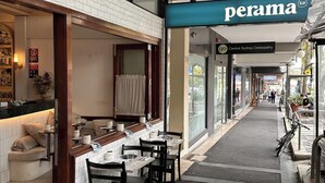 A restaurant with a tiled wall, a counter with stools, and a sign for 'perama 2.0 Central Sydney Osteopathy'. - MetaWiseBnB Spacious Apartment – 6km to CBD (Petersham)