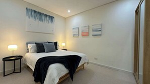 A bedroom with a bed, two bedside tables with lamps, a large abstract painting, and three smaller paintings on the wall. - MetaWiseBnB Spacious Apartment – 6km to CBD (Petersham)