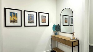 A hallway with three framed travel posters, a mirror, and a wooden console table with decorative items. - MetaWiseBnB Spacious Apartment – 6km to CBD (Petersham)