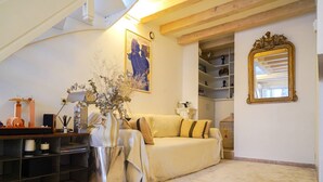 Uma sala de estar aconchegante com sofá, um vaso decorativo, uma estante de livros e um quadro na parede.