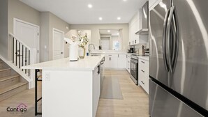 Une cuisine moderne avec des meubles blancs, un réfrigérateur en acier inoxydable et un îlot central.