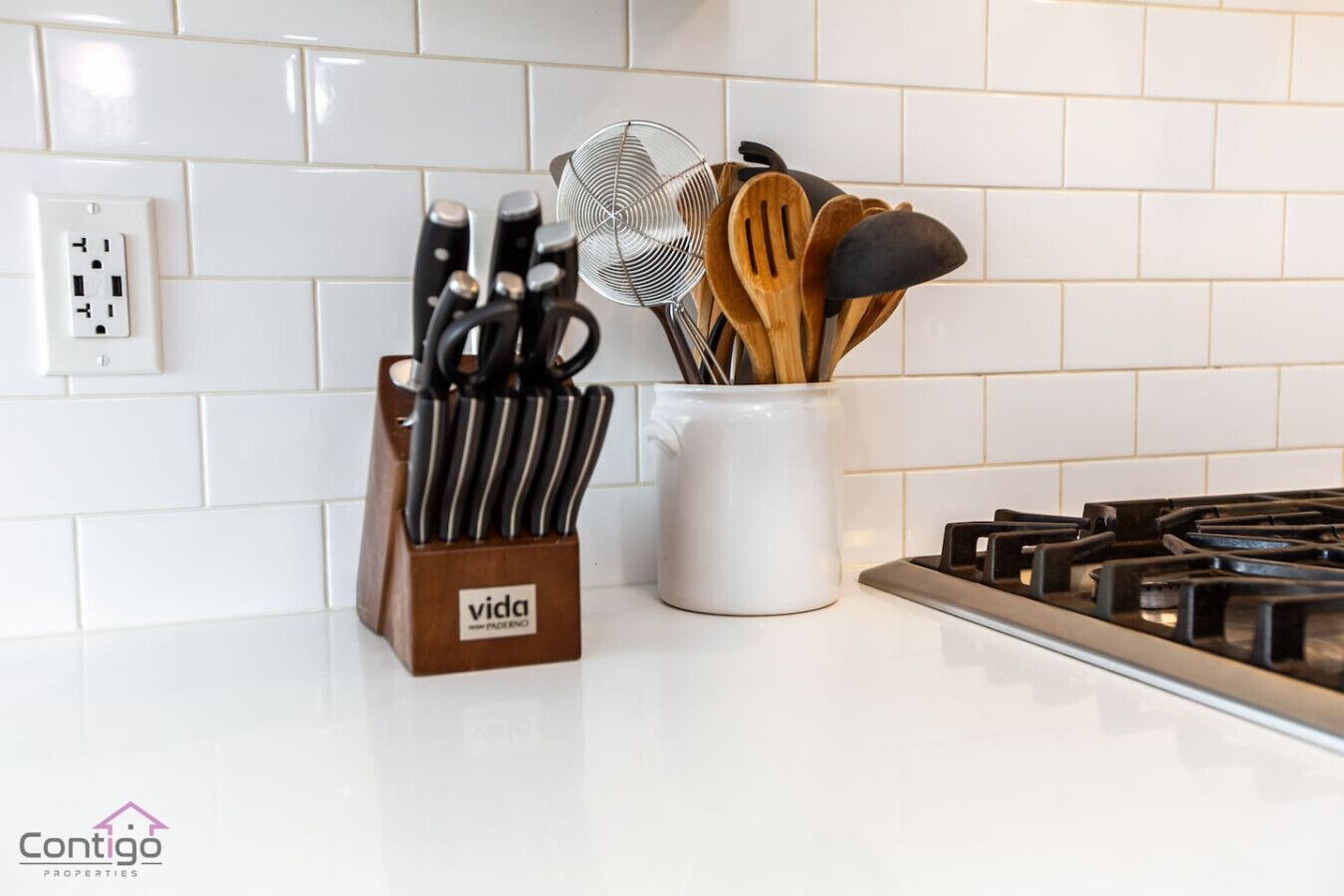 A kitchen counter with a knife block, a strainer, and wooden utensils.