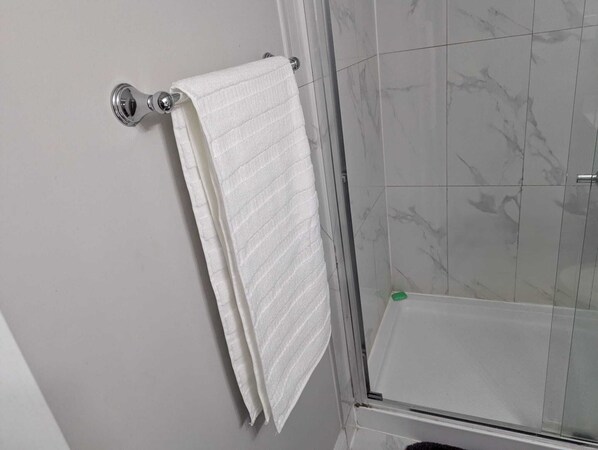 Une salle de bain avec une serviette blanche suspendue à une barre à serviettes métallique, une douche en verre et des murs à motifs de marbre.