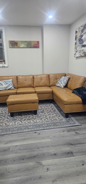 Um sofá modular com um banquinho, um tapete estampado e um quadro na parede.