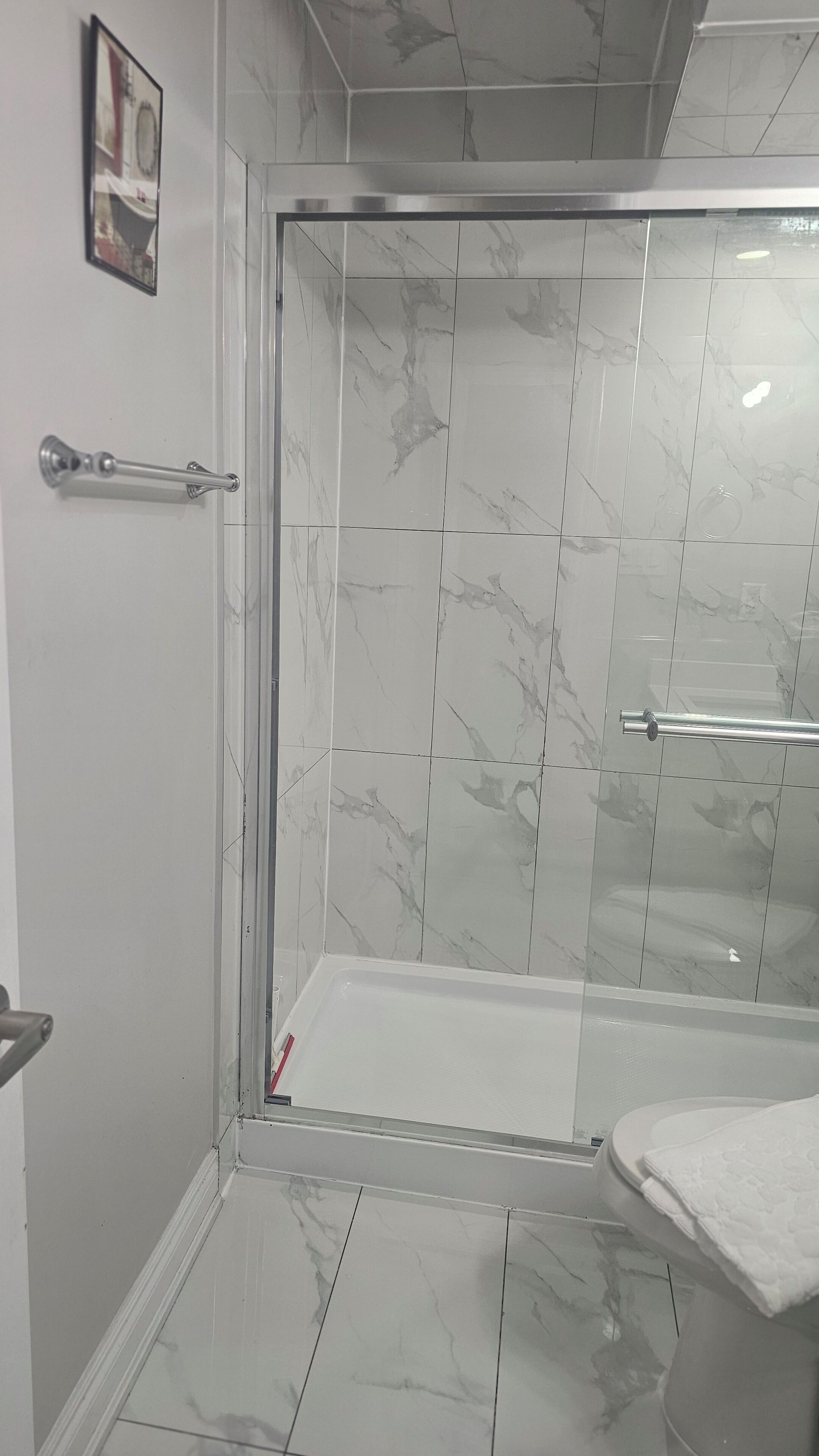 A bathroom with a glass shower enclosure, marble tiles, and a towel rack.