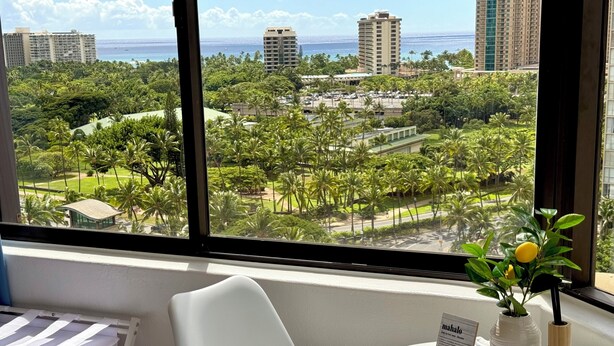 A hotel room with a large window offering a view of a cityscape and palm trees. - Cozy Ocean-view studio in the heart of Waikiki (Honolulu)
