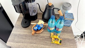 A coffee maker, a kettle, two water bottles, and a wooden tray with snacks on a wooden table. - Cozy Ocean-view studio in the heart of Waikiki (Honolulu)