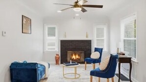 Una sala de estar con chimenea, un sofá azul, un sillón azul y un ventilador de techo.