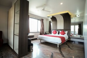 Une chambre d’hôtel moderne avec un grand lit, un ventilateur de plafond, une fenêtre avec des rideaux, une table de chevet ronde et un miroir.