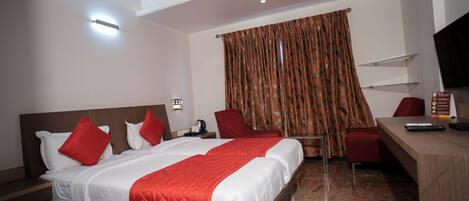 A hotel room with a bed, two red chairs, a desk, a television, and a ceiling fan.