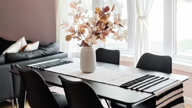 A dining area with a table set for four, a vase with dried flowers, and a sofa in the background. - Spacious 3BR Home with Fast Wi-Fi and Free Parking (Winnipeg)