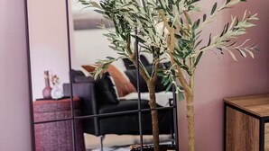 A room with a large mirror, two potted olive trees, a black sofa, and a wooden cabinet. - Spacious 3BR Home with Fast Wi-Fi and Free Parking (Winnipeg)