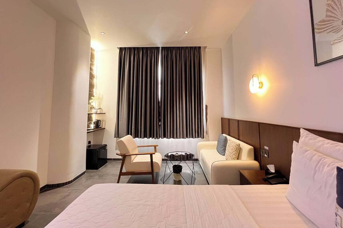 Une chambre d’hôtel comprenant un lit, un canapé, une chaise, une table basse, un bureau, une lampe et une fenêtre avec des rideaux.