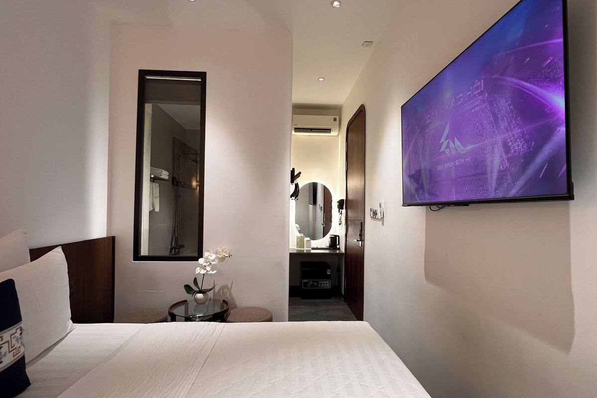 Une chambre d’hôtel avec un lit, un grand miroir, une télévision et une petite table sur laquelle se trouve un vase.