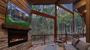 Eine Holzterrasse mit Kamin aus Stein, Sitzgelegenheit und Blick auf einen Wald.