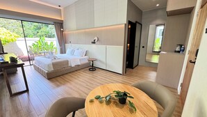 A modern hotel room with a bed, a small round table with chairs, a desk, and a view of greenery outside. - Tambuna Retreat & Events (Ipoh)