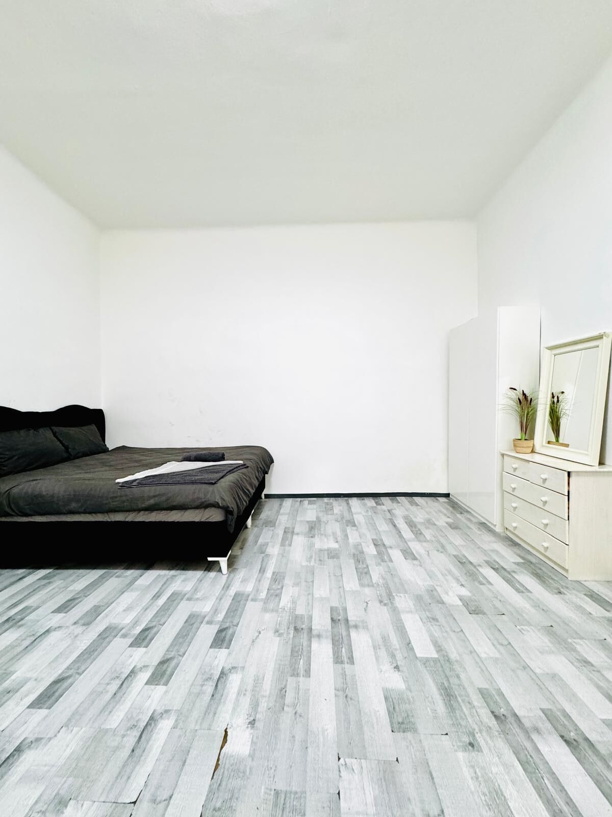 A minimalist bedroom with a bed, a dresser, and a mirror.
