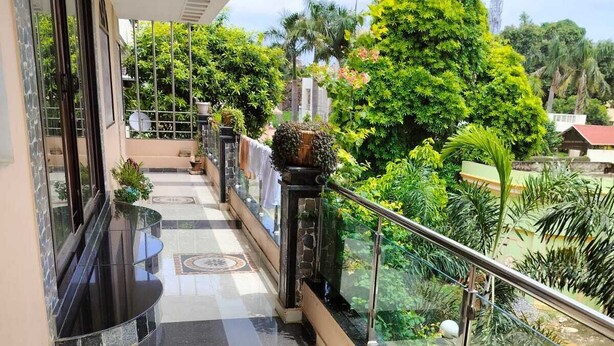 A balcony with a tiled floor, glass railing, and potted plants. - Pratimalaya Inn Guest House (Varanasi)