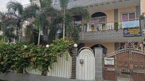A two-story building with a gated entrance, a balcony with plants, and a sign indicating it is a guest house. - Pratimalaya Inn Guest House (Varanasi)