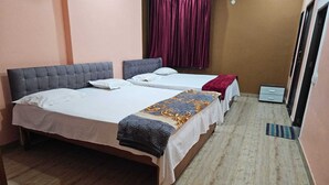 A small, clean room with two beds, a wooden floor, and a window with curtains. - Pratimalaya Inn Guest House (Varanasi)