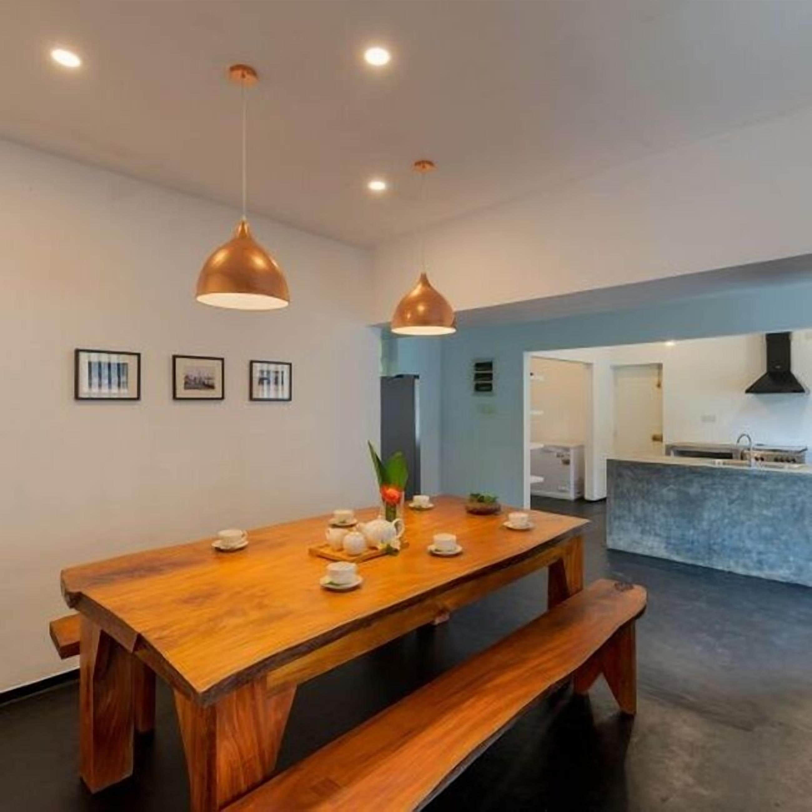 A modern kitchen with a wooden dining table, pendant lights, and a bench.