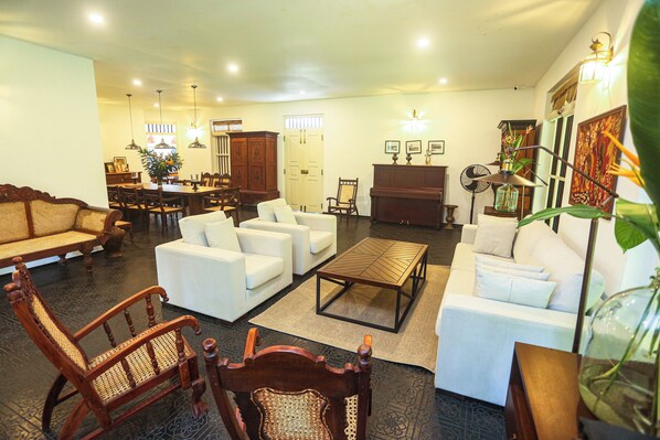 A spacious living room with a dining area, a piano, and a large plant.