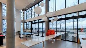 Un grand espace intérieur doté de larges fenêtres, d’une table de ping-pong et de sièges orange.