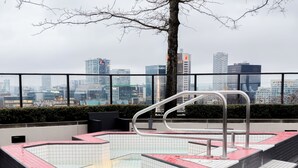 Un espace piscine sur le toit, offrant une vue sur le paysage urbain, avec une échelle en métal et un sol carrelé en noir et rouge.