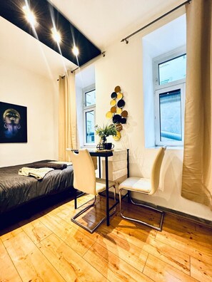 Una habitación pequeña con cama, una mesita y una planta, una silla y un adorno en la pared.
