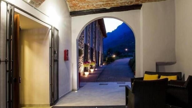 An arched corridor with a view of a mountain at dusk, leading to a building with a door and a small outdoor seating area. - hotel palas (Bruzolo)