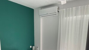 En snyggt bäddad säng med ett grått överkast, två kuddar med prickigt mönster och en hög med hopvikta handdukar.